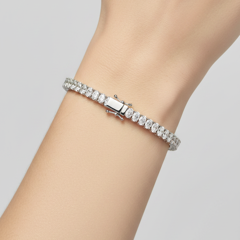 Female model wearing white gold oval-cut diamond tennis bracelet with four-prong settings