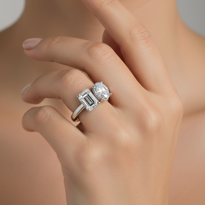 Female model wearing white gold two-stone toi-et-moi ring with large vertical emerald-cut diamond on the left and large vertical oval-cut diamond on the right side by side in four-prong settings on a slim plain white gold band