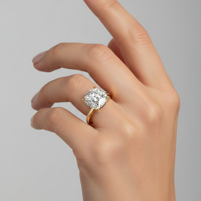 Female model wearing yellow gold cushion-cut diamond solitaire engagement ring with four rounded ball-tipped claw prongs at each corner and smooth plain high-polish yellow gold rounded band
