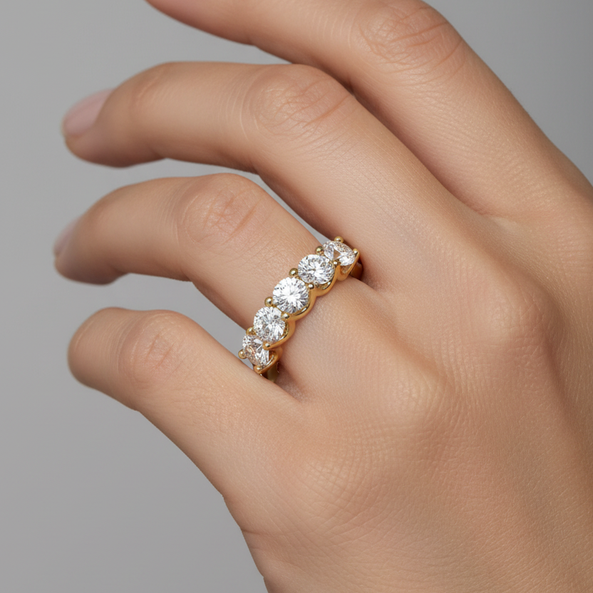 Female model wearing yellow gold seven-stone round brilliant diamond half-eternity band with seven large equal-sized diamonds in scalloped ball-tipped four-prong settings across the top of the finger on a smooth plain yellow gold band