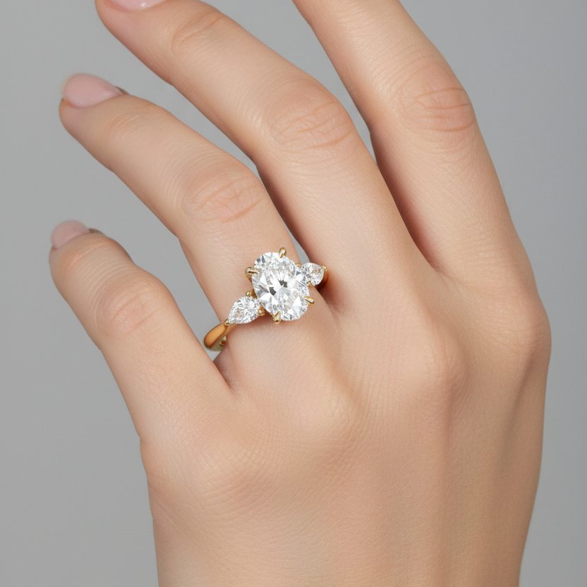 Female model wearing yellow gold three-stone diamond engagement ring with oval center and pear side stones