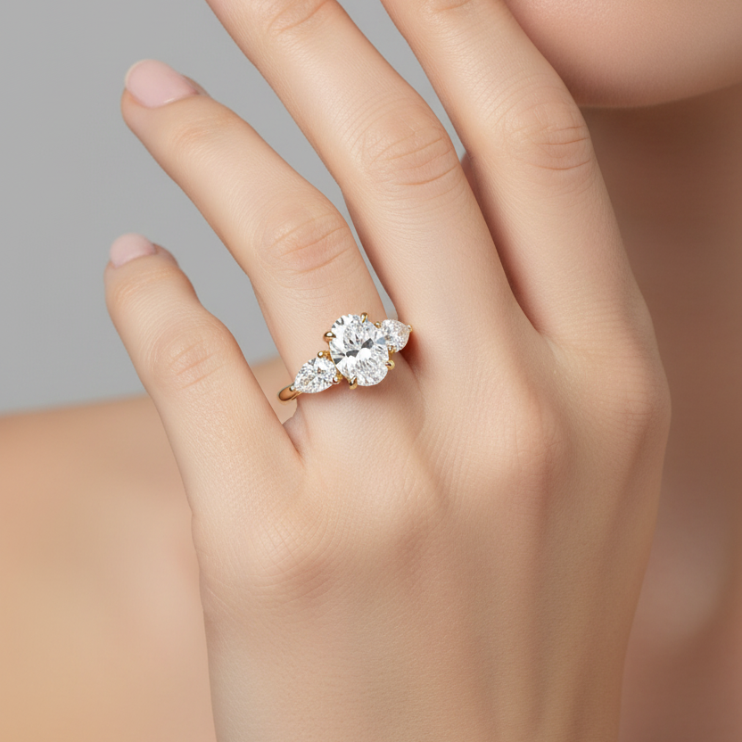 Female model wearing yellow gold three-stone diamond engagement ring with oval center and pear side stones