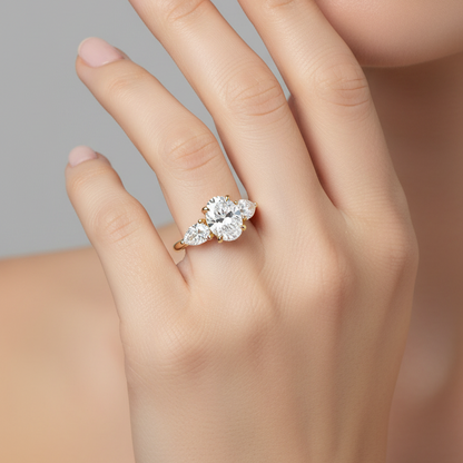 Female model wearing yellow gold three-stone diamond engagement ring with oval center and pear side stones