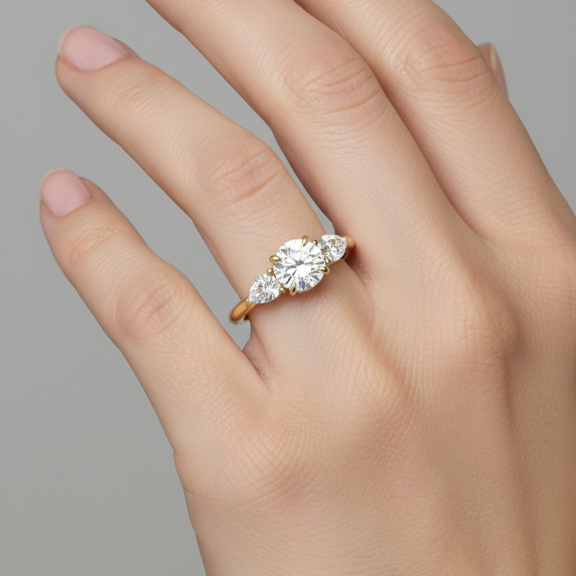 Female model wearing yellow gold three-stone diamond engagement ring with round brilliant center and pear side stones top-down view