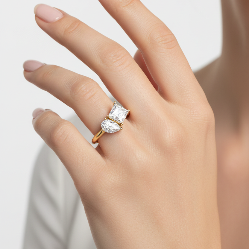 Female model wearing yellow gold toi et moi two-stone ring with princess-cut and pear-cut diamonds