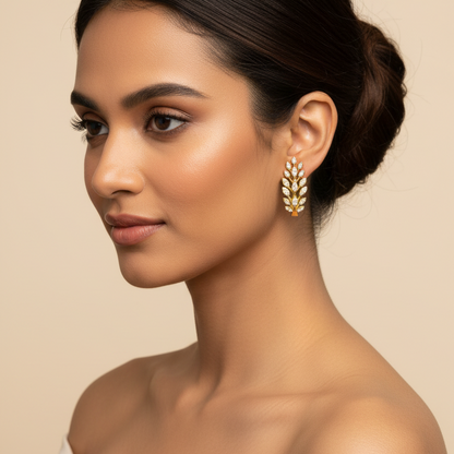 A woman in profile wearing a gold leaf-shaped drop earring with white stones, set against a warm beige background.