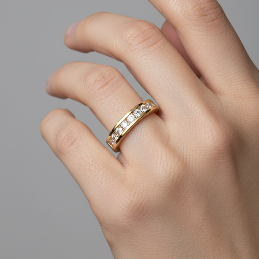 Female model's hand wearing a very small yellow gold channel-set diamond half eternity band ring with a moderately wide smooth polished yellow gold band featuring a recessed channel groove running along the top center flanked by two parallel raised yellow gold rails holding approximately 16-20 round brilliant diamonds of uniform size set flush and level within the channel covering half to three-quarters of the band circumference the sides and inner shank being smooth plain polished yellow gold