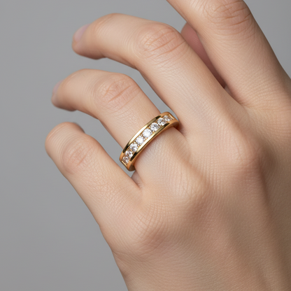 Female model's hand wearing a very small yellow gold channel-set diamond half eternity band ring with a moderately wide smooth polished yellow gold band featuring a recessed channel groove running along the top center flanked by two parallel raised yellow gold rails holding approximately 16-20 round brilliant diamonds of uniform size set flush and level within the channel covering half to three-quarters of the band circumference the sides and inner shank being smooth plain polished yellow gold