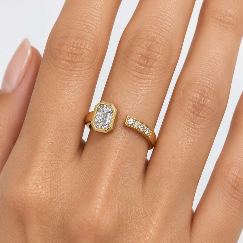 Female model's hand wearing a very small yellow gold open bypass cuff ring with two open ends facing each other — the left end rising to a bold architectural stepped octagonal full yellow gold bezel housing a large emerald-cut diamond flush within the multi-stepped chamfered frame sparkling with beautiful flashes of light and the right end curving up to a smooth flat rectangular yellow gold tip set with four small round brilliant diamonds in shared pavé prong settings the smooth wide plain polished yellow g