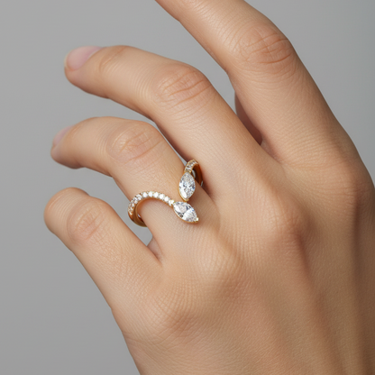 A close-up of a hand wearing a gold ring with marquise-cut clear stones, set against a solid gray background.