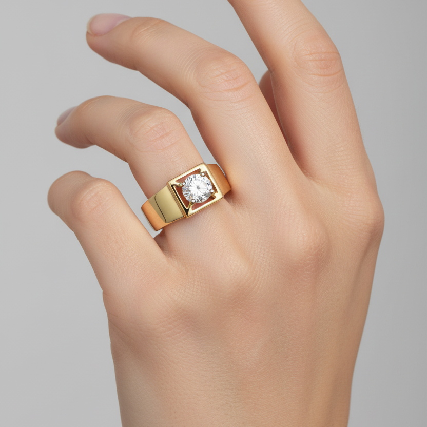 Female model's hand wearing a very small yellow gold wide-band solitaire ring with a broad smooth high-mirror-polish yellow gold band and a bold square architectural yellow gold box frame at the top center holding a large round brilliant diamond in four white gold ball-tipped prongs at each corner of the square the round brilliant nearly filling the square opening and sparkling brilliantly the warm yellow gold wide band contrasting distinctively with the bright white gold ball-tipped prongs