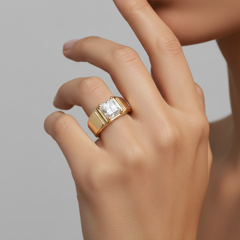 A close-up of a hand wearing a yellow gold ring with a rectangular clear gemstone, set against a neutral gray background.