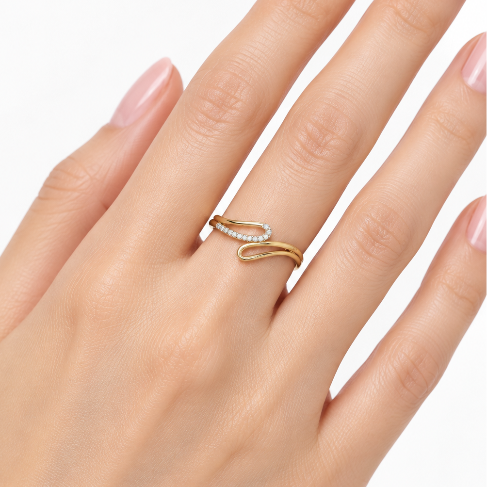 Female model's hand with light porcelain skin and soft blush manicure wearing a very small yellow gold wave swirl bypass ring featuring a smooth wide plain polished yellow gold bar arm sweeping diagonally from lower left to upper right and a curved pavé diamond arc arm curving upward and to the left in a graceful concave crescent wave shape with a continuous single row of round brilliant diamonds in shared pavé prong settings along the full length of the curved arc the two arms interlocking and overlapping 