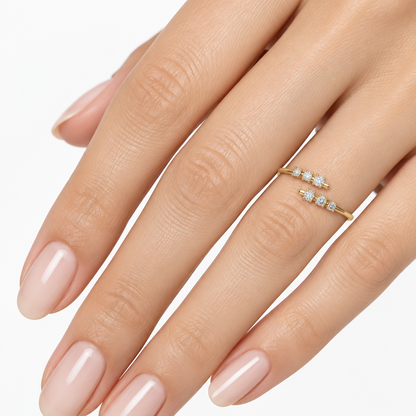 Female model's hand with light warm skin and nude manicure wearing a very small yellow gold open bypass ring with two parallel graduating diamond rows — one arm curving upward terminating in three round brilliant diamonds graduating from smallest at the tip to largest toward the center each in individual four-prong rounded yellow gold claw settings and the other arm curving from below terminating in a mirrored row of three similarly graduating round brilliant diamonds both arms facing each other at the top 