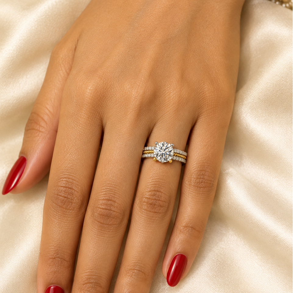 Female model's hand with warm golden Indian skin and classic red nail polish wearing a very small yellow gold and white gold triple-row diamond solitaire ring with a wide band featuring a top row of round brilliant pavé diamonds in white gold settings a center twisted yellow gold rope braid texture row and a bottom row of round brilliant pavé diamonds in white gold settings with a large round brilliant diamond in six mixed white and yellow gold ball-tipped prong settings rising prominently above the band th
