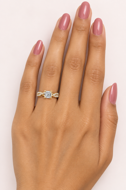 Female model's hand with warm golden Indian skin and rose-tinted nail polish wearing a very small yellow gold Asscher-cut diamond solitaire engagement ring with a twisted infinity pavé band featuring one smooth plain polished yellow gold strand and one double-row round brilliant diamond pavé strand spiraling and intertwining like an infinity knot with X-shaped crossover points on each shoulder clustered with pavé diamonds meeting at four large rounded yellow gold ball-tipped claw prongs holding a large Assc