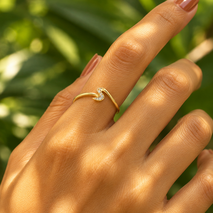 Female model's hand with warm golden Indian skin and soft warm terracotta caramel manicure wearing a very small yellow gold sculptural wave ring — a smooth plain polished yellow gold band sweeping up at the center top into a fluid S-shaped zigzag wave silhouette with a small cluster of round brilliant diamonds in shared pavé prong settings nestled within the inner concave curve of the wave peak the rest of the ring entirely plain smooth polished yellow gold minimal architectural and fluid — a pure gold wave