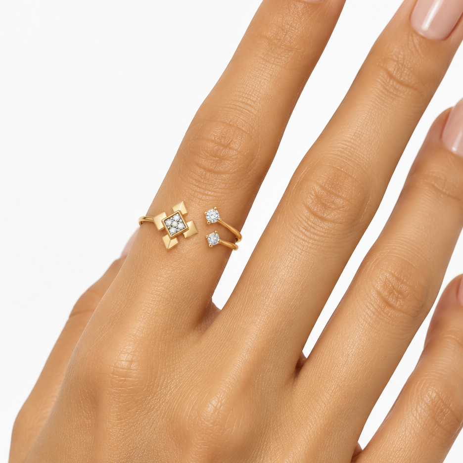 Female model's hand with warm golden skin and nude manicure wearing a very small yellow gold open bypass ring with a geometric star cross diamond motif — a bold square motif rotated 45 degrees with four pointed yellow gold arrow spike tips extending north south east west in a compass cross pattern with the square face fully pavé set with a cluster of sparkling diamonds on one end and the band splitting into two thin parallel yellow gold wires each tipped with a single floating round brilliant diamond in a t