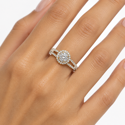 Female model's hand with warm light golden skin and nude manicure wearing a very small yellow gold round brilliant halo engagement ring with a split-shank double pavé band featuring a bold circular halo of round brilliant diamonds in shared pavé yellow gold prong settings in a perfect circle around a large elevated round brilliant-cut diamond in four yellow gold claw prong settings rising above the halo plane sparkling with exceptional brilliance below which the band splits into two separate parallel arms e