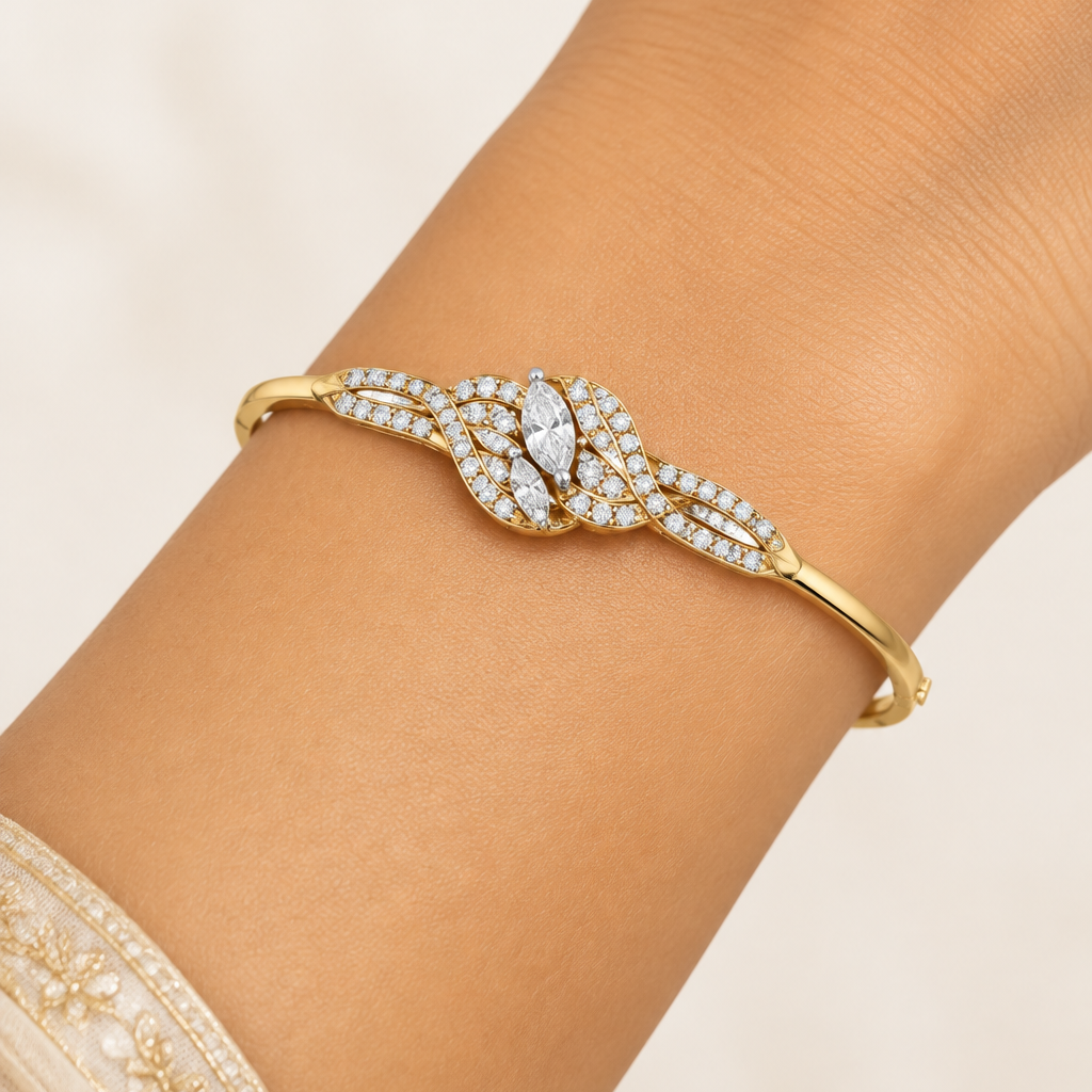 Female model's slender wrist with warm golden Indian skin wearing a very small yellow gold diamond bangle bracelet with an elaborate floral knot centerpiece featuring multiple curved flowing yellow gold strands interweaving like leaves and petals each set with a continuous row of round brilliant pavé diamonds with two marquise-cut diamonds at the very center of the knot in white gold claw prong settings sparkling brilliantly with pointed oval shapes the slim plain high-mirror polished yellow gold bangle for