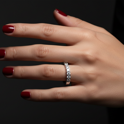 Generated dramatic cinematic studio editorial variation - beautiful Indian female model wearing the white gold round brilliant diamond half-eternity wedding band, strong directional side light against near-black background with face-on overhead angle showing the full spectacular continuous arc of graduating round brilliant diamonds blazing with extraordinary icy prismatic fire and cool silver-white rim light on the smooth plain white gold lower band, deep red nails and dark navy sleeve