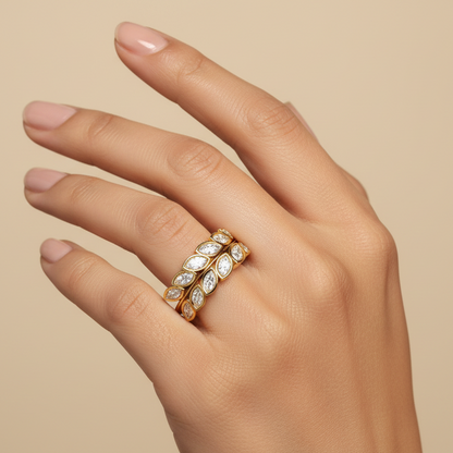 Generated fresh variation - Indian female model wearing the yellow gold double-row bezel-set marquise and round brilliant diamond botanical leaf band ring, warm golden hour backlit lighting on champagne background