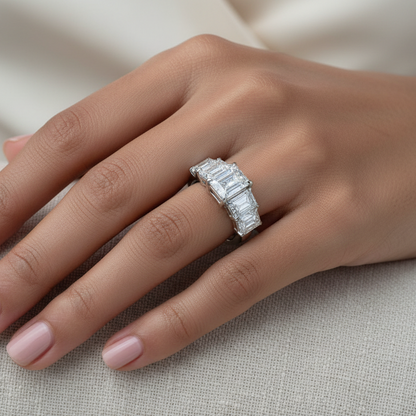 Generated image of a beautiful Indian female model wearing the white gold five-stone emerald-cut diamond engagement ring with spectacular large radiant-cut diamond centre flanked by two graduating emerald-cut diamonds on each side in a beautiful continuous five-stone inline cluster on a smooth wide plain white gold shank