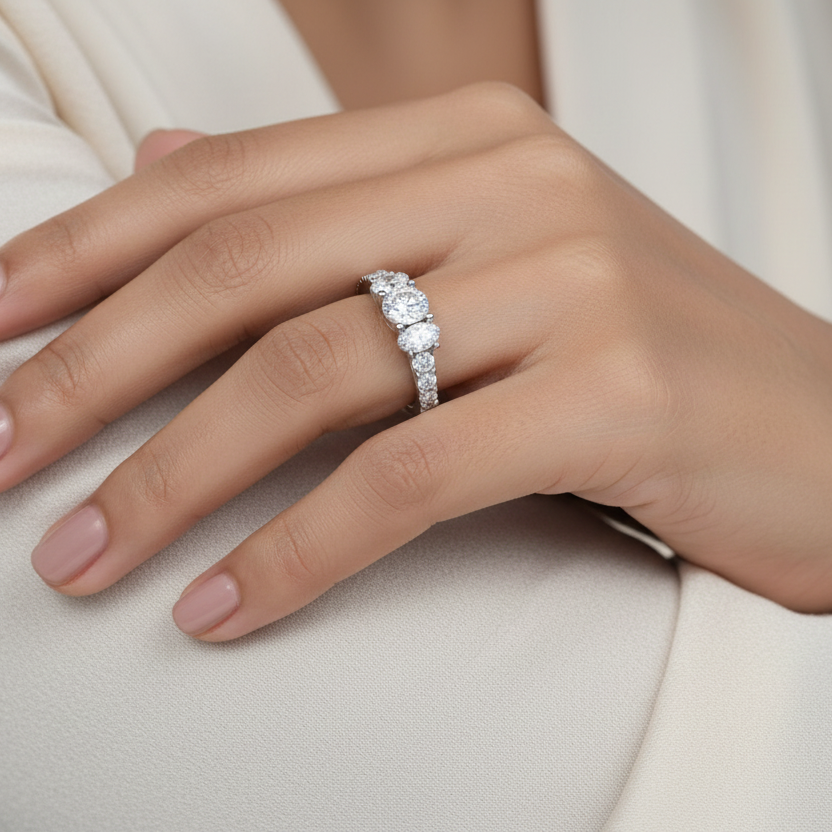 Generated image of a beautiful Indian female model wearing the white gold three oval-cut diamond cluster ring with graduating alternating oval and round brilliant diamond shoulders — three closely set oval-cut diamonds in the centre cluster with spectacular graduating diamond-set shoulders running along both sides of the shank all blazing simultaneously with extraordinary icy white fire and rainbow scintillation