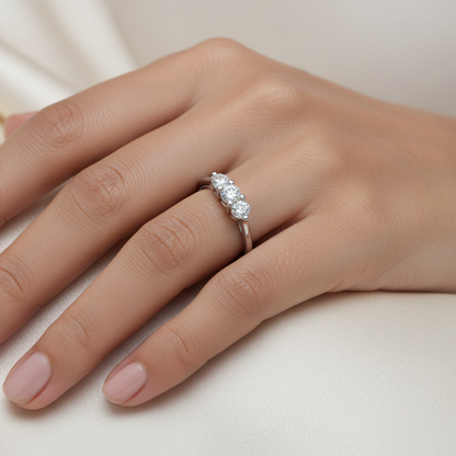Generated image of a beautiful Indian female model wearing the white gold three-stone round brilliant diamond trilogy ring with three equal-sized round brilliant diamonds in beautiful shared flat-bar white gold claw settings sitting closely together in a tight three-diamond cluster on a smooth wide plain white gold shank all blazing simultaneously with extraordinary icy white fire and rainbow scintillation
