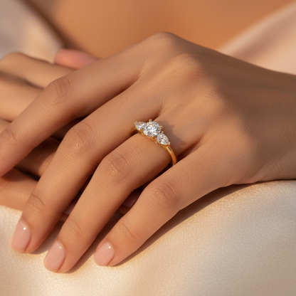 Generated image of a beautiful Indian female model wearing the yellow gold round brilliant diamond trilogy engagement ring with large round brilliant centre diamond in six-claw setting flanked by two substantial pear-cut diamond side stones with rounded bases nestling close to the centre in a beautiful tight three-stone cluster on a smooth wide plain yellow gold shank