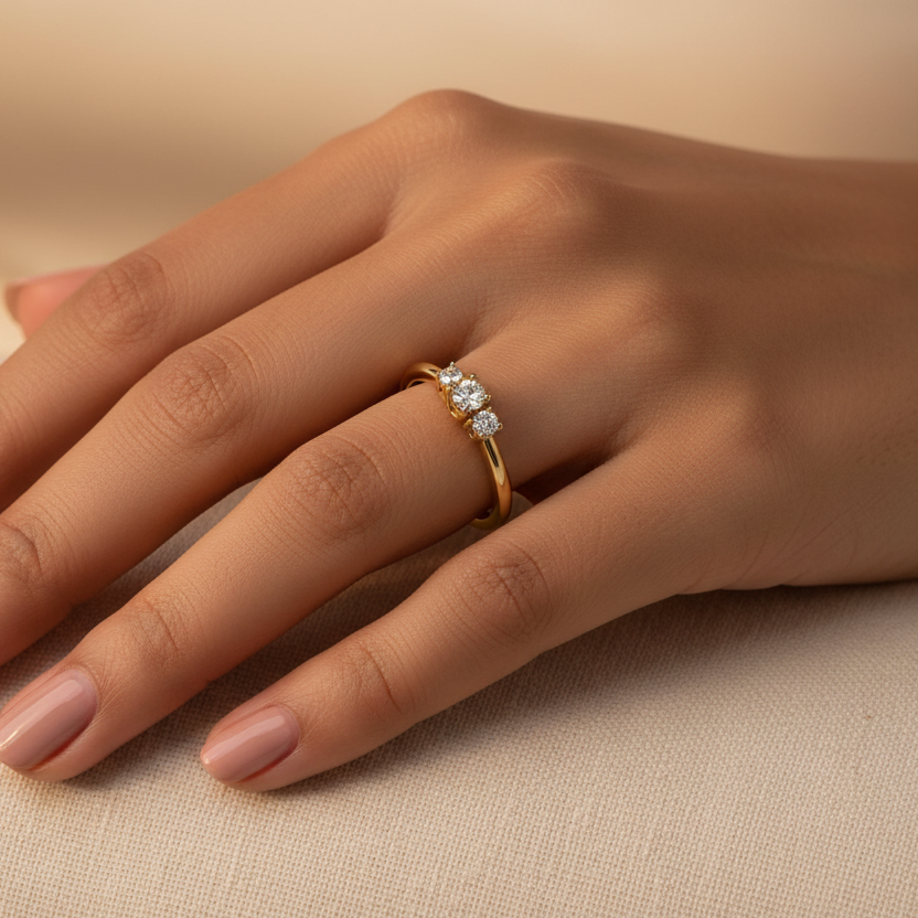 Generated image of a beautiful Indian female model wearing the yellow gold three-stone round brilliant diamond trilogy ring with medium round brilliant centre diamond flanked by two smaller round brilliant side stones in a beautiful petite shared-claw trilogy setting on a smooth slim plain yellow gold shank