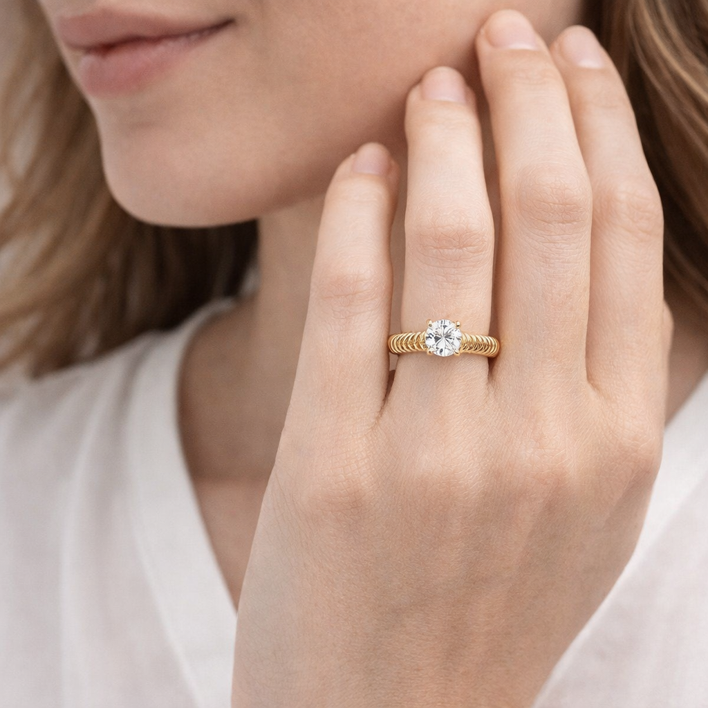 Close-up of a hand wearing a gold ring with a diamond on a neutral background