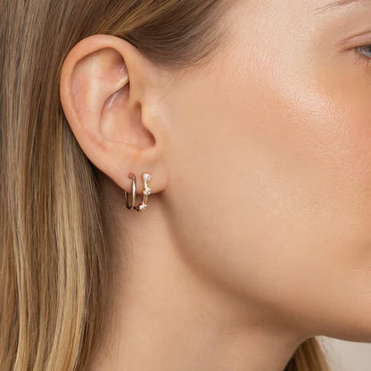 Close-up of a person wearing gold hoop earrings with small clear stones.