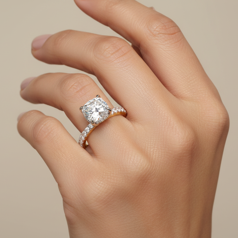 Generated image of an Indian female model wearing the two-tone yellow gold and white gold four-prong cushion-cut diamond solitaire engagement ring with hidden micro-pavé halo under-gallery and pavé diamond shoulders