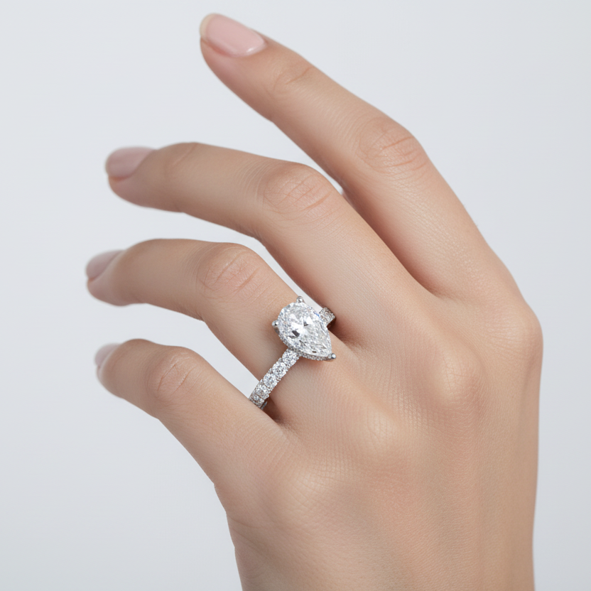Generated image of an Indian female model wearing the white gold five-prong pear-cut solitaire engagement ring with hidden micro-pavé halo under-gallery and large round brilliant pavé diamond band