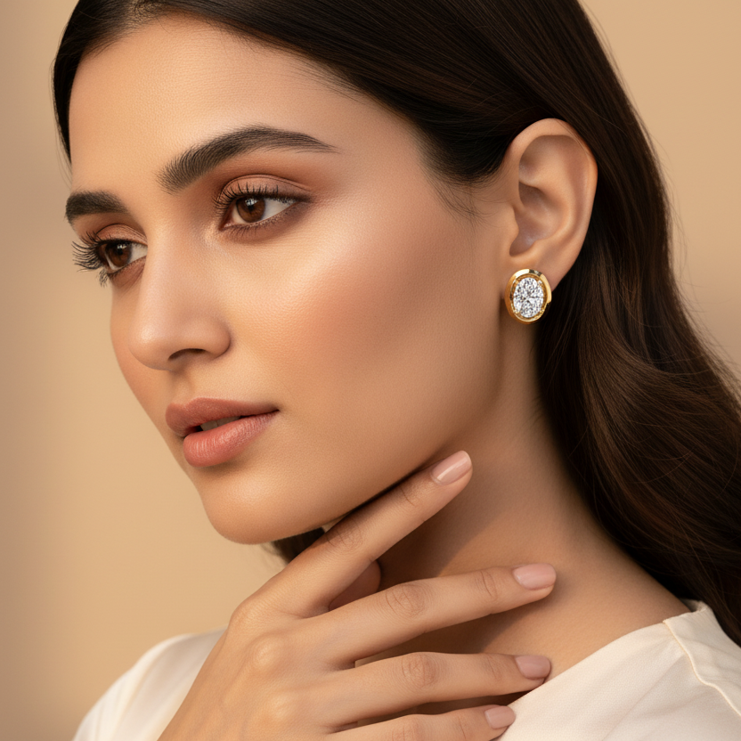 Generated very small dainty size variation - beautiful Indian female model wearing the yellow gold oval-cut diamond solitaire stud earrings with wide flat oval bezel frame as extremely tiny delicate petite accent studs, warm golden hour light on champagne background with soft romantic waves hairstyle and ivory silk outfit