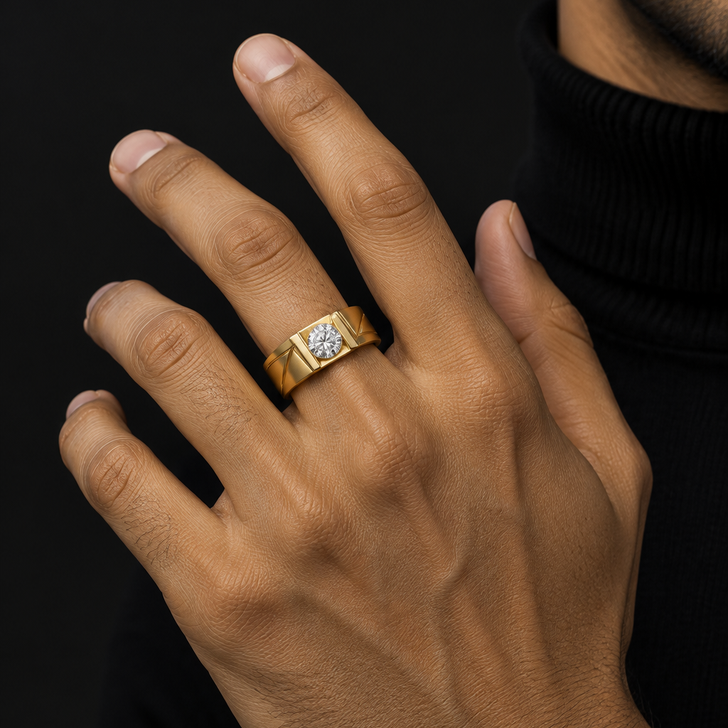 Handsome elegant Indian male model's hand with warm golden skin and well-groomed clean short nails wearing a very small wide yellow gold men's solitaire ring with geometric angular relief groove texture — wide flat polished yellow gold band with subtle diagonal angular relief grooves or geometric cuts carved into the face creating a bold textured pattern; round brilliant diamond set low and proud directly into the band in a gypsy flush-bezel yellow gold setting deeply integrated into the face of the wide ba