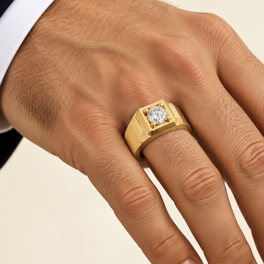 Handsome elegant male model's strong well-groomed hand with light olive skin tone wearing a very small yellow gold heavy men's signet-style solitaire ring with a wide bold chunky high-mirror polished yellow gold band featuring dramatic deep angled step-cut geometric grooves on each side creating a stepped plinth shoulder effect with a square recessed platform at the center top housing a large round brilliant diamond in four yellow gold ball-tipped prong settings sparkling brilliantly viewed from a 3/4 side 