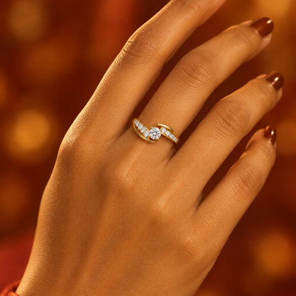 Indian female model's hand with warm golden skin and deep rich cognac warm caramel brown manicure wearing a very small yellow gold round brilliant diamond solitaire ring with a dramatic diagonal crossover bypass diamond band — band splitting into two sweeping diagonal arms crossing past each other in opposite directions around the center stone both arms channel-set with round brilliant diamonds running diagonally; center round brilliant diamond in a four-prong yellow gold tension-style setting held between 