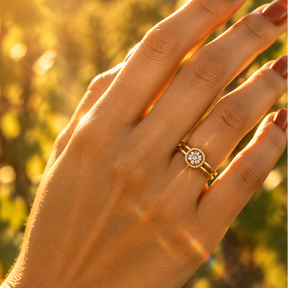 Indian female model's hand with warm golden skin and deep rich terracotta burnt orange manicure wearing a very small yellow gold round brilliant diamond solitaire double-shank rope bezel ring — a split double-band shank with two parallel smooth rounded plain polished yellow gold bands converging at the center top into a circular round bezel frame with a decorative twisted rope braided yellow gold border within which a large round brilliant diamond solitaire sparkles brilliantly catching warm golden hour lig
